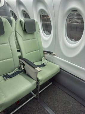Modern bir yolcu uçağının modern uçak kabininde yan yana iki yeşil eko-deri koltuk. Pencereleri pencereli, temiz, minimalist iç tasarım. Hava yolculuğu, konfor, yolculuk, ulaşım ve yeni bir maceranın başlangıcı.