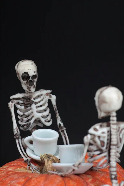 Concetto di Halloween - due scheletri che bevono tè sul tavolo di zucca sullo sfondo nero. Immagine verticale — Foto Stock