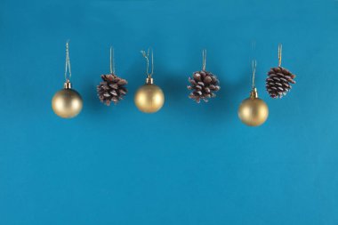 Mavi arka planda izole edilmiş altın Noel baloları ve köknar kozalakları. Noel dekorasyonu konsepti. Uzayı kopyala Yatay resim