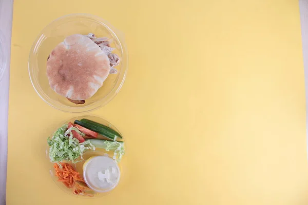 Plastik kasede bir jiroskoplu sandviç. Ekmek ve jiroskopu sarı arka planda izole etmek için malzemeler. Resim kopyalama alanı içeriyor