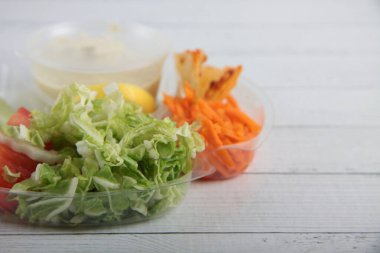 Dükkan teslimatı konsepti. Beyaz ahşap arka planda bir kasede salata malzemeleri. Resim kopyalama alanı içeriyor