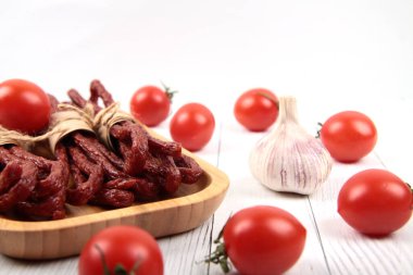 Kabanos or cabanossi - traditional Polish thin dry smoked sausage made of beef and herbs, Cherry tomatoes and garlic on white wooden background. Image contains copy space