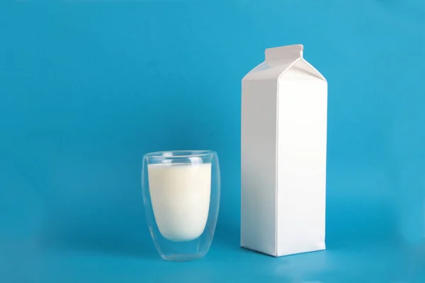 fermented milk concept - white pack and glass of kephir isolated on blue background. Image contains copy space
