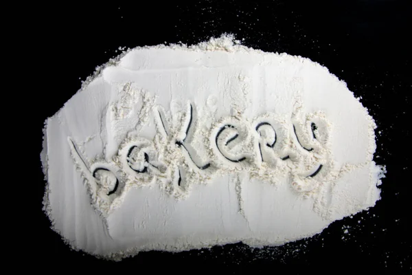 inscription Bakery made on flour against black background flat lay