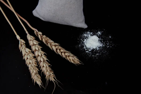 Bag with flour and three ears of wheat isolated on black background flat lay. Image contains copy space