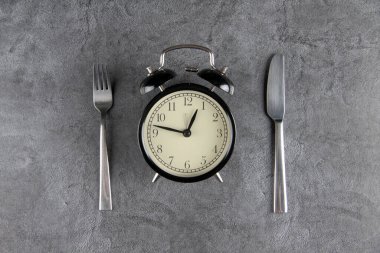 Gri arka planda izole edilmiş çalar saat, çatal ve masa bıçağı. Resim kopyalama alanı içeriyor