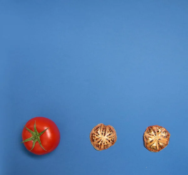 fresh tomato and dried tomato isolated on blue background flat lay. Image contains copy space