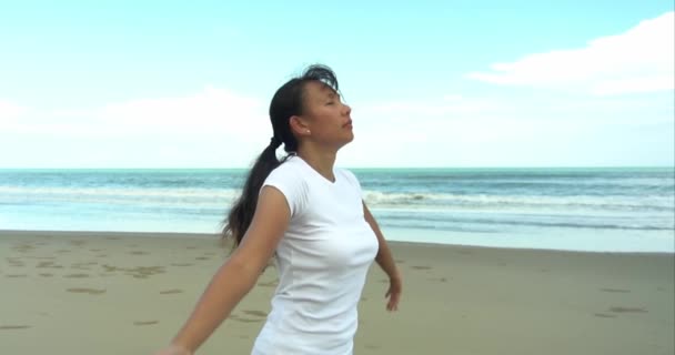 スローモーション 白スポーツウェアの健康的で美しいアジアの女性が手を上げ 熱帯ビーチで瞑想のためにヨガを練習します — ストック動画