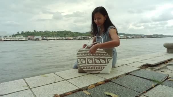 Bonita Chica Asiática Sentada Orilla Del Río Sacando Bolso Bolsa — Vídeos de Stock