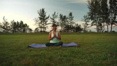 Dışarıda oturan ve kulaklıkla yoga yapan bir kadın - fitness insanları ve müzik kavramı