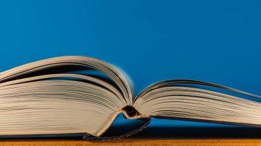 Kavisli sayfaları olan açık bir kitap meşe ağacından bir masanın mavi arka planında yatıyor. Tasarım için arka plan. Web pankartı.
