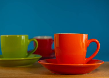 turuncu, yeşil, kırmızı çay tabağı mavi arka planda, ahşap bir masanın üzerinde duruyor. Tasarım için.