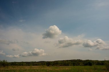 Mavi gökyüzünde bulutlar, yaprak döken orman ve çayır. Bahar mevsimi.