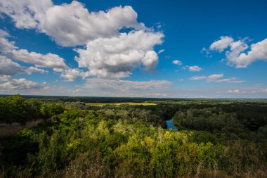 Mavi gökyüzünde, ormanda ve çayırlarda beyaz bulutlar. Köyde yaz günü.