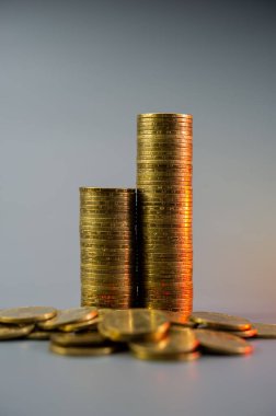 Yükselen sırayla iki altın para yığını ve açık gri arka planda duran bozuk paralar. İş konsepti. Kapak.