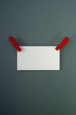 Bir tane boş kartvizit ve mandallar gri arka planda yatıyor. Kapak.