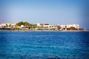 Güneşli bir günde, arka planda bir grup otelle aydınlık deniz kenarı