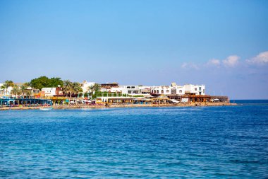 Güneşli bir günde, arka planda bir grup otelle aydınlık deniz kenarı