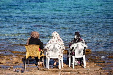Denizin kenarında oturan üç Müslüman kadın, Dahab, Sina, Mısır