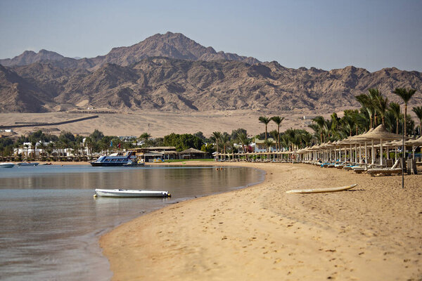 Пустые шезлонги с зонтиками у моря, горы на заднем плане