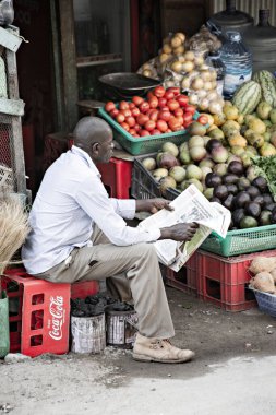 WATAMU, KENYA - Aralık 2020: Afrikalı adam Watamu, Kenya 'da pazarda meyve satıyor ve gazete okuyor