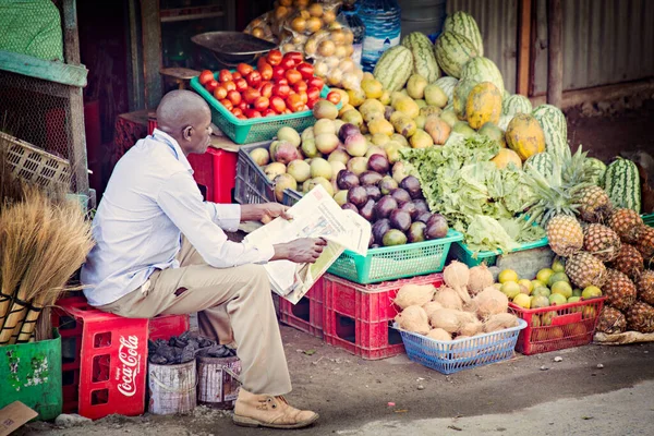 WATAMU, KENYA - Aralık 2020: Afrikalı adam Watamu, Kenya 'da pazarda meyve satıyor ve gazete okuyor