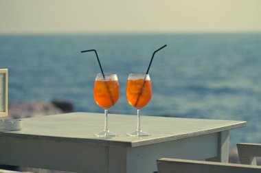 İki Aperol Spritz kokteyli denizin önündeki masada.