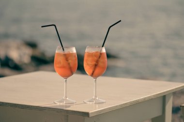 İki Aperol Spritz kokteyli denizin önündeki masada.