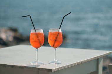 İki Aperol Spritz kokteyli denizin önündeki masada.