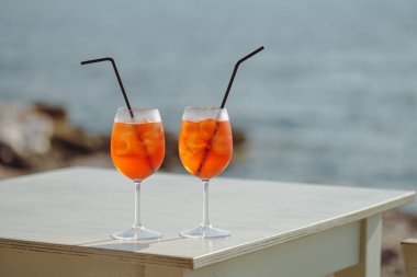 İki Aperol Spritz kokteyli denizin önündeki masada.