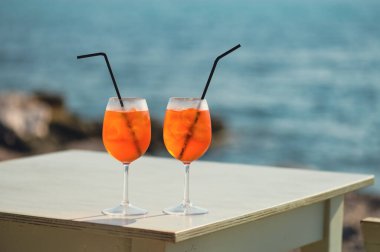İki Aperol Spritz kokteyli denizin önündeki masada.