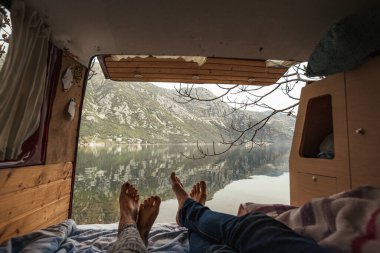 Kamp minibüsü içeride, karavanda göl manzarasının tadını çıkaran bir çift.