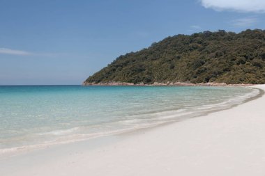 Beyaz kum ve turkuaz su dalgalarıyla güzel bir sahil akıyor.