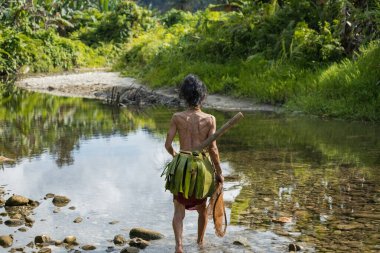 SIBERUT, INDONESIA - 5 Kasım 2025: Mentawai kabilesindeki geleneksel kıyafet ve vücut süslemeleri giyen kadın, Siberut Adası 'ndaki köyünde nehirde balık tutarken fotoğraflandı, Sumatra, Endonezya