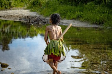 SIBERUT, INDONESIA - 5 Kasım 2025: Mentawai kabilesindeki geleneksel kıyafet ve vücut süslemeleri giyen kadın, Siberut Adası 'ndaki köyünde nehirde balık tutarken fotoğraflandı, Sumatra, Endonezya