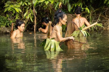 SIBERUT, INDONESIA - 5 Kasım 2025: Mentawai kabilesindeki geleneksel kıyafet ve vücut süslemeleri giyen kadın, Siberut Adası 'ndaki köyünde nehirde balık tutarken fotoğraflandı, Sumatra, Endonezya