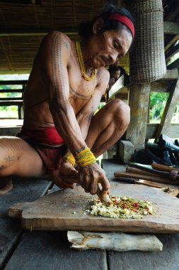SIBERUT, INDONEZYA - 5 Kasım 2025: Geleneksel giysi ve vücut dekorasyonlarıyla Mentawai şamanı zehri Siberut adası Batı Sumatra Endonezya 'daki evinde avlanmak için hazırlıyor