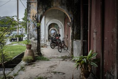 PAPAN, MALAYSIA - 10 Kasım 2025: Papan Heritage Village 'deki eski sömürge dönemi koridoru, soyulmuş boyalar, fazla gelişmiş bitkiler, ve bu tarihi Malezya yerleşim bölgesinin terk edilmiş ama atmosferik cazibesini artıran eski bir rattan sandalyesi