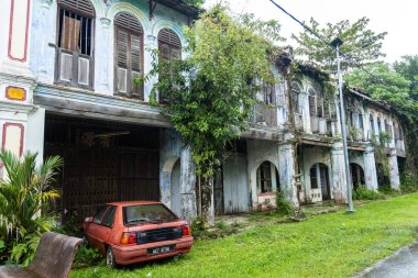 PAPAN, MALAYSIA - 10 Kasım 2025: Papan Heritage Village 'deki eski sömürge dönemi koridoru, soyulmuş boyalar, fazla gelişmiş bitkiler, ve bu tarihi Malezya yerleşim bölgesinin terk edilmiş ama atmosferik cazibesini artıran eski bir rattan sandalyesi