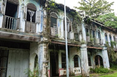 PAPAN, MALAYSIA - 10 Kasım 2025: Papan Heritage Village 'deki eski sömürge dönemi koridoru, soyulmuş boyalar, fazla gelişmiş bitkiler, ve bu tarihi Malezya yerleşim bölgesinin terk edilmiş ama atmosferik cazibesini artıran eski bir rattan sandalyesi