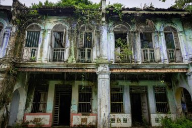PAPAN, MALAYSIA - 10 Kasım 2025: Papan Heritage Village 'deki eski sömürge dönemi koridoru, soyulmuş boyalar, fazla gelişmiş bitkiler, ve bu tarihi Malezya yerleşim bölgesinin terk edilmiş ama atmosferik cazibesini artıran eski bir rattan sandalyesi