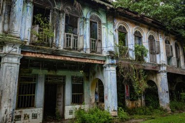 PAPAN, MALAYSIA - 10 Kasım 2025: Papan Heritage Village 'deki eski sömürge dönemi koridoru, soyulmuş boyalar, fazla gelişmiş bitkiler, ve bu tarihi Malezya yerleşim bölgesinin terk edilmiş ama atmosferik cazibesini artıran eski bir rattan sandalyesi