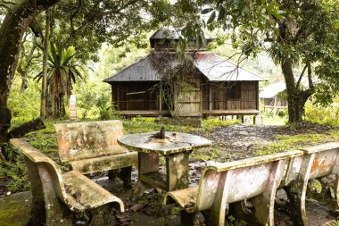 PAPAN, MALAYSIA - 10 Kasım 2025: Papalık Mirası Köyü 'nde geleneksel bir ahşap cami olan tarihi Lama Papan' a bakan yemyeşil ağaçların altındaki eski yosun kaplı taş banklar ve masa