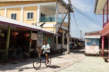 PULAU KETAM, MALAYSIA - 30 Kasım 2025: Pulau Ketam Malezya balıkçı köyündeki dar sokakta bisiklet süren adam