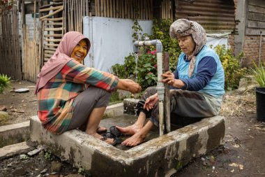 BERASTAGI, İNDONEZYA - 15 Kasım 2025: Kuzey Sumatra Endonezya köyündeki su kuyusunda yıkanan iki Endonezyalı kadın