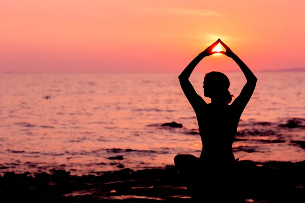 Woman silhouette sitting in lotus position on sea background back lit — Stock Photo, Image