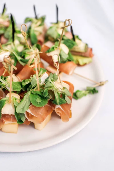 Jambonlu kanepeler, peynirli peynirler, yakın plan beyaz tabakta şiş roka..