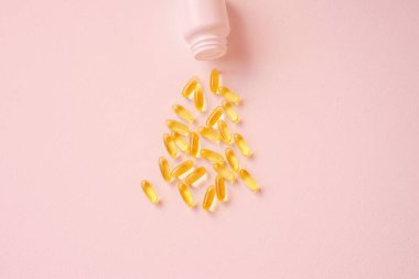 Birçok tablet plastik bir konteynere dökülür. Hastalık tedavisi kavramı. Yakın plan, pembe tarafsız arkaplan manzaralı. Vitamin tedavisi, balık yağı, D vitamini..