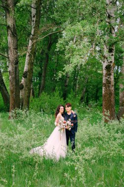 Düğün günü. Genç mutlu yeni evliler taze yeşil ormanda. Gelin ve damadın portresi. Bahar düğünü. Uluslararası çift. Açık havada düğün töreni..