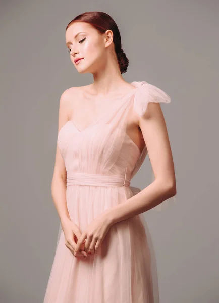 Bridesmaid\'s dresses. Elegant moscato dress. Beautiful pink chiffon evening gown. Studio portrait of young happy ginger woman. Transformer dress idea for an event.